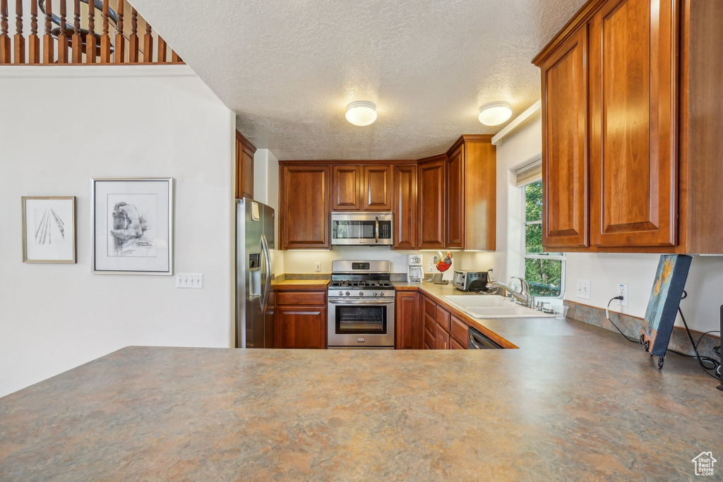 Kitchen featuring appliances with stainless steel finishes, a sink, a textured ceiling, and brown cabinets