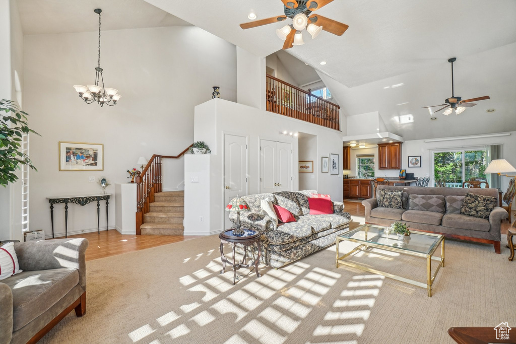 Living room featuring a ceiling fan, high vaulted ceiling, stairs, a chandelier, and light colored carpet