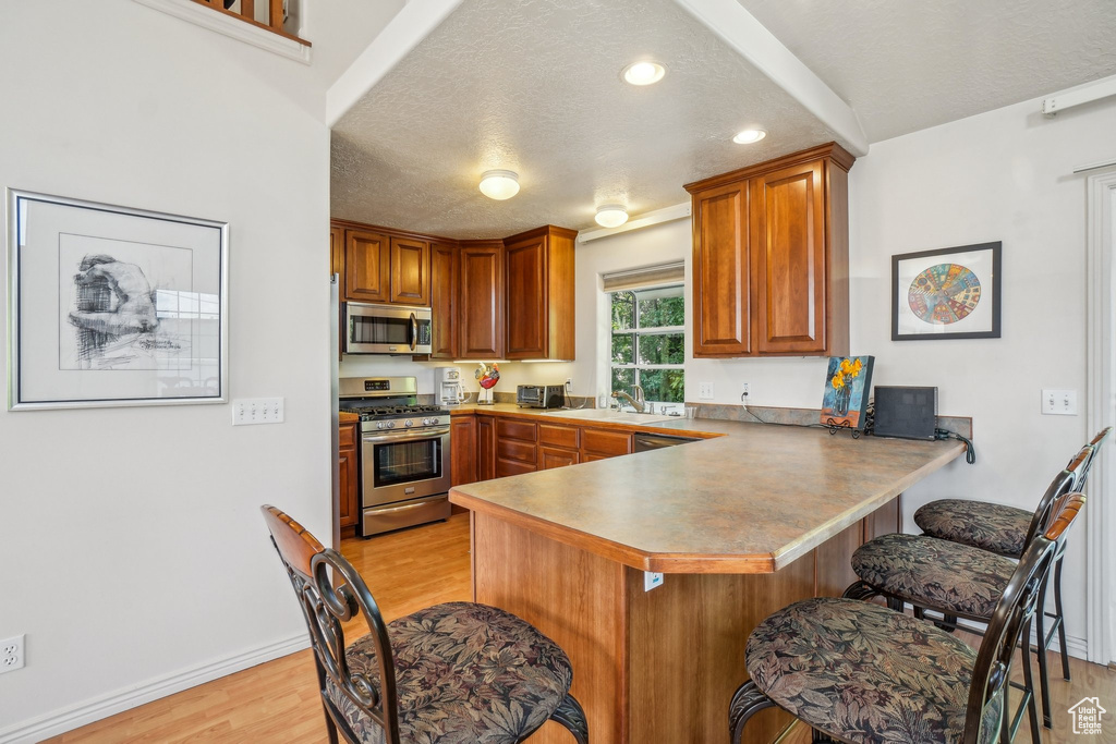 Kitchen with stainless steel appliances, a textured ceiling, light wood-style flooring, a peninsula, and a breakfast bar