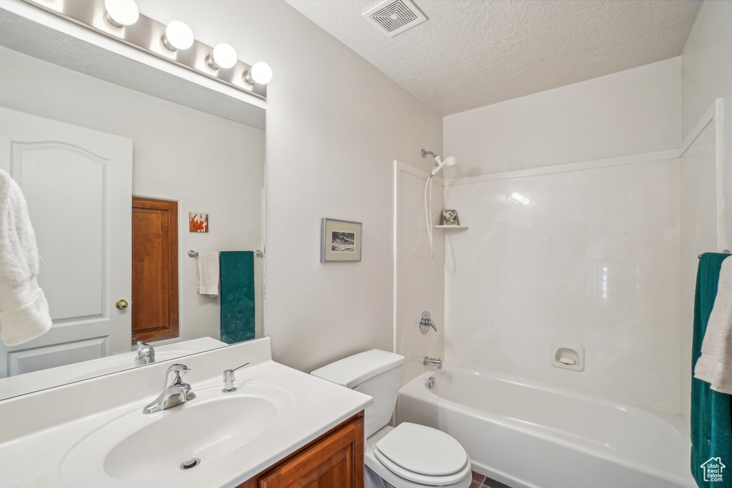 Full bathroom with vanity, bathing tub / shower combination, toilet, and a textured ceiling