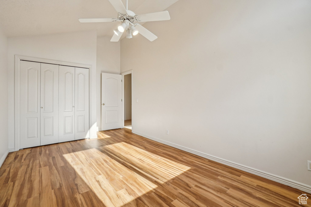 Unfurnished bedroom with baseboards, wood finished floors, a closet, a ceiling fan, and high vaulted ceiling