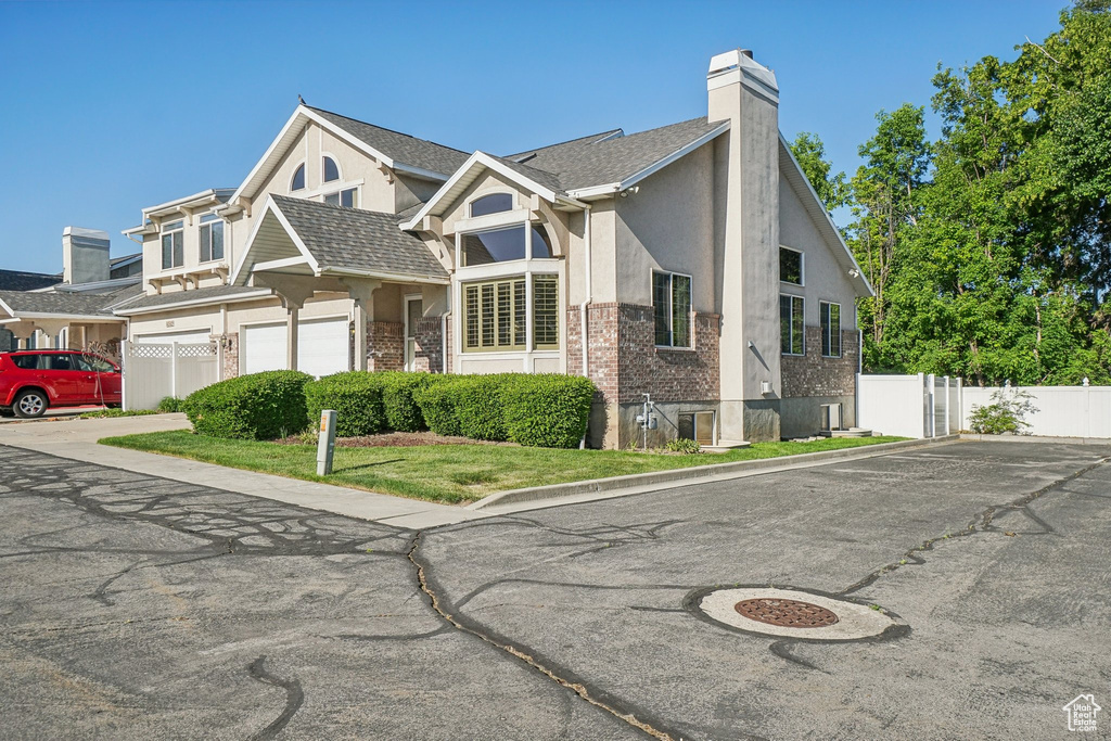View of front of home with a chimney, stucco siding, brick siding, a garage, and driveway