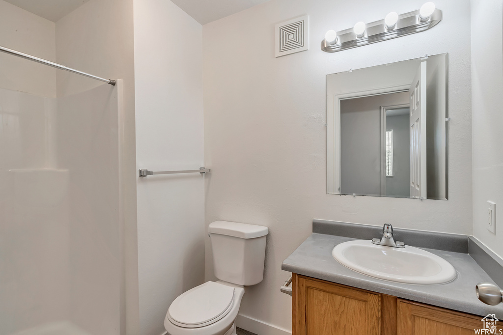 Bathroom featuring toilet, a shower, and vanity