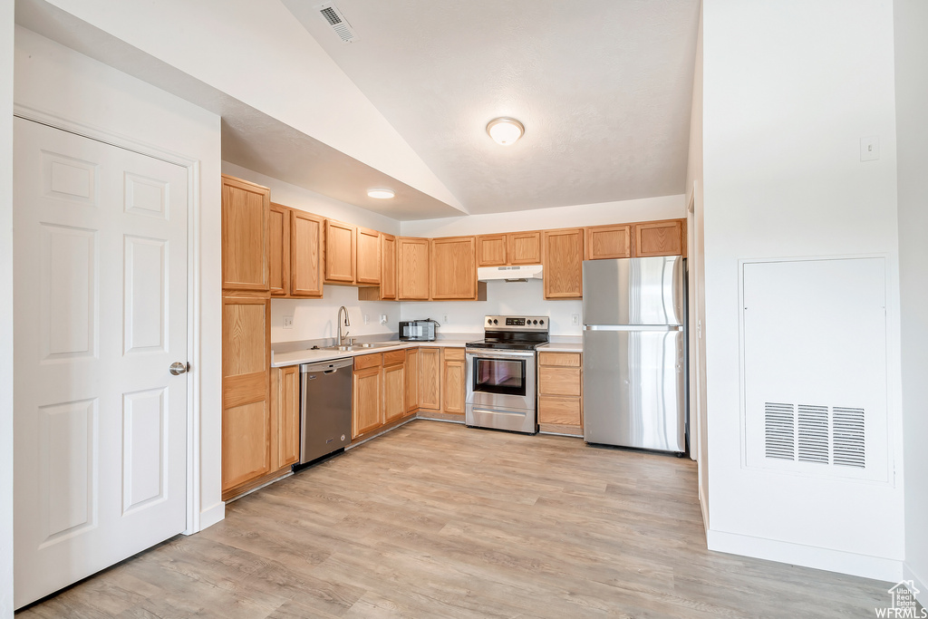 Kitchen featuring stainless steel appliances, under cabinet range hood, vaulted ceiling, light countertops, and a sink