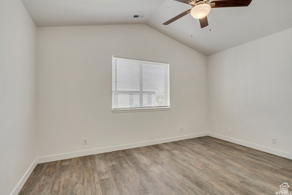Spare room featuring a ceiling fan, wood finished floors, vaulted ceiling, and baseboards