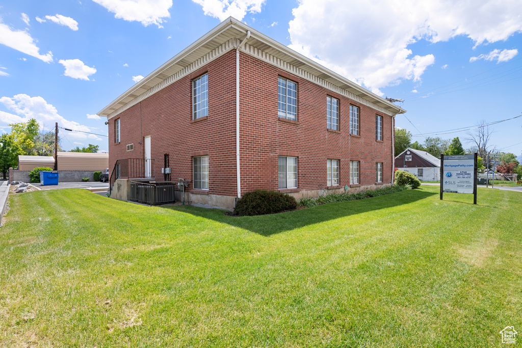 View of side of property with a yard, brick siding, and central air condition unit