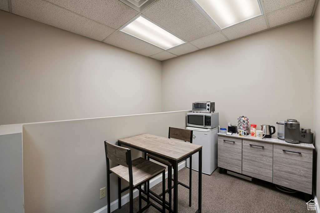 Kitchen featuring a drop ceiling, dark colored carpet, stainless steel microwave, light countertops, and refrigerator