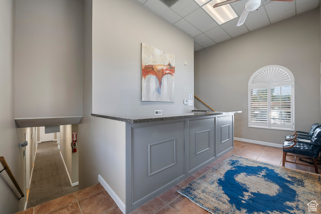 Misc room with a drop ceiling, ceiling fan, baseboards, light tile patterned flooring, and an upstairs landing