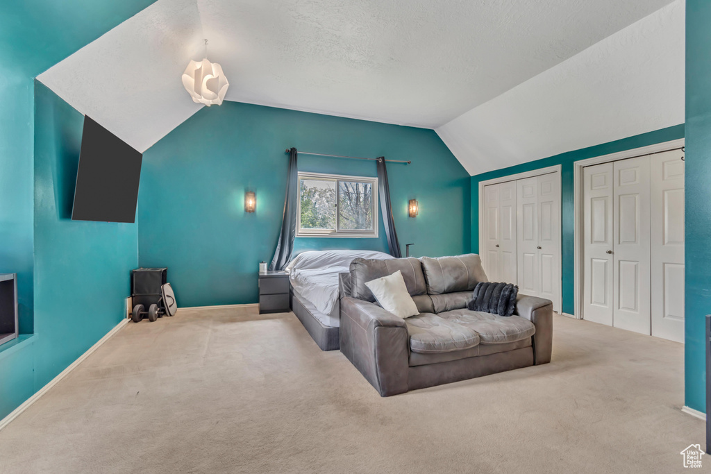 Carpeted bedroom featuring multiple closets, vaulted ceiling, and baseboards