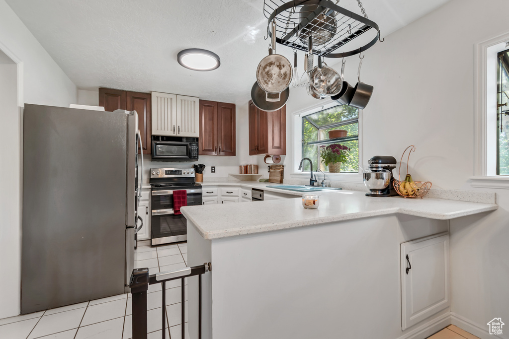 Kitchen featuring stainless steel appliances, a sink, a peninsula, and light tile patterned flooring