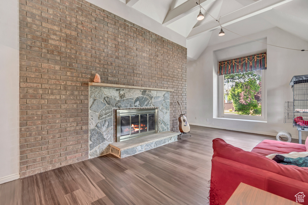 Living area with vaulted ceiling, a large fireplace, wood finished floors, and baseboards