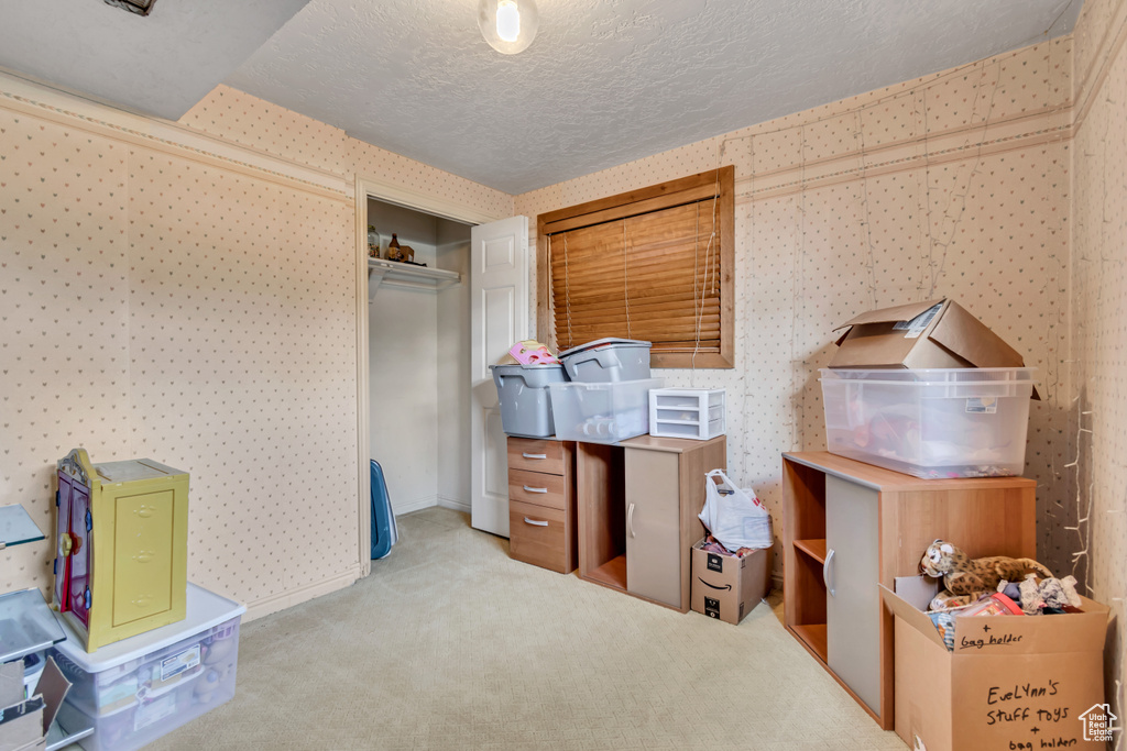 Carpeted bedroom with wallpapered walls, a textured ceiling, and a closet