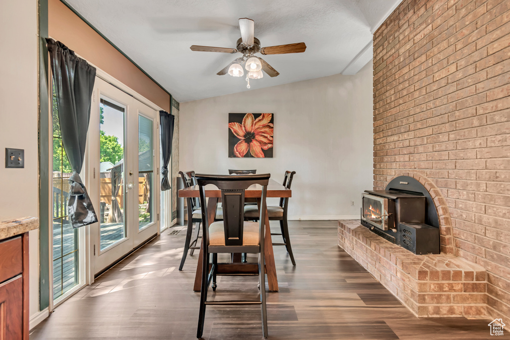 Dining room featuring a wood stove, healthy amount of natural light, a ceiling fan, dark wood-style flooring, and brick wall