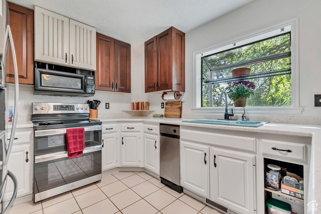 Kitchen featuring appliances with stainless steel finishes, a sink, light countertops, white cabinets, and light tile patterned floors