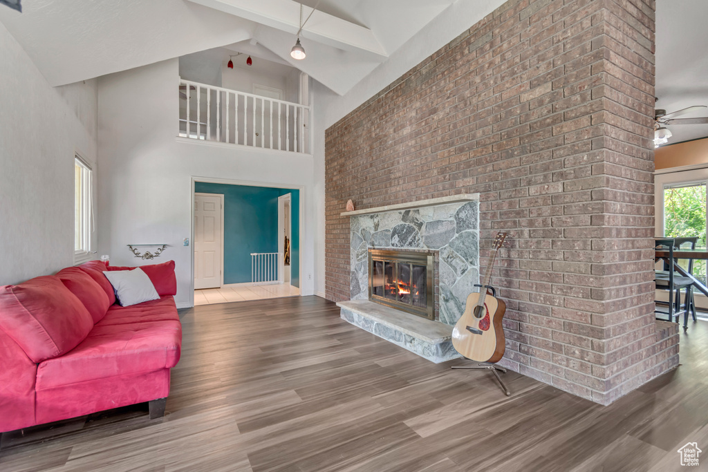 Living area with wood finished floors, a stone fireplace, high vaulted ceiling, radiator heating unit, and beamed ceiling