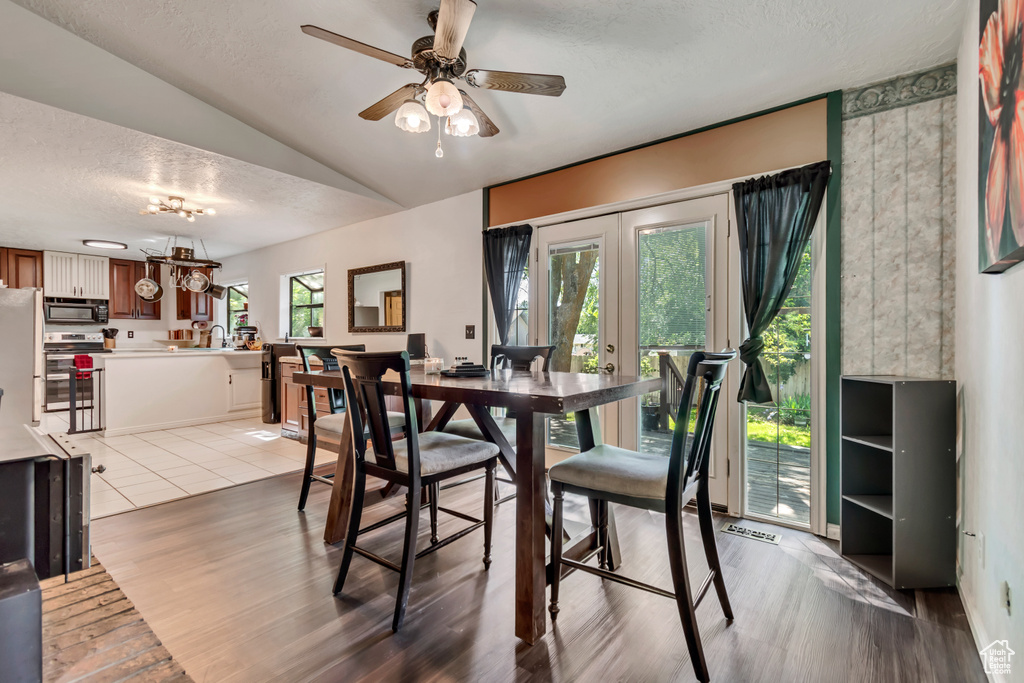 Dining space with a textured ceiling, lofted ceiling, ceiling fan, light wood-type flooring, and french doors