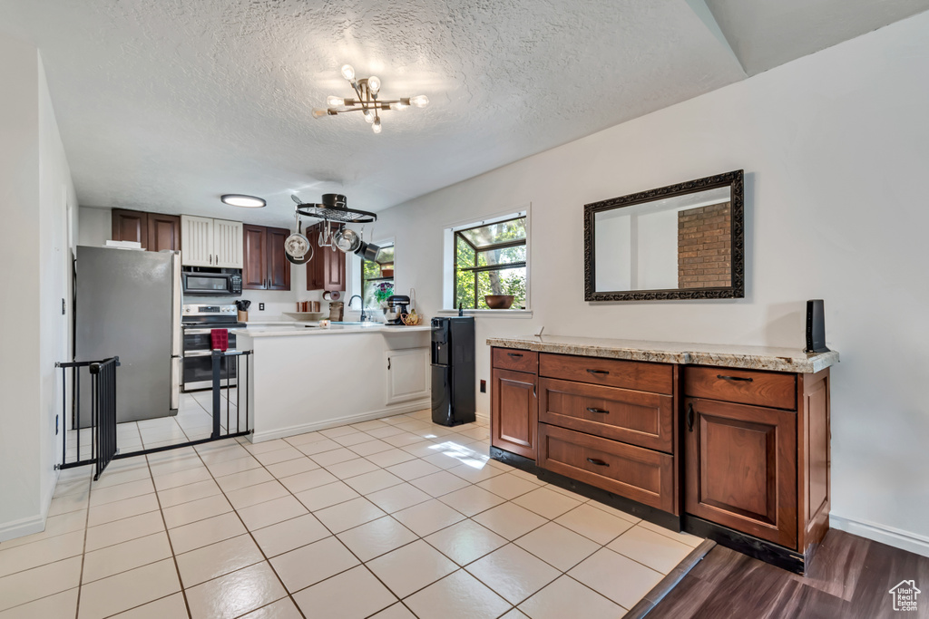 Kitchen with stainless steel appliances, light countertops, a chandelier, a textured ceiling, and baseboards
