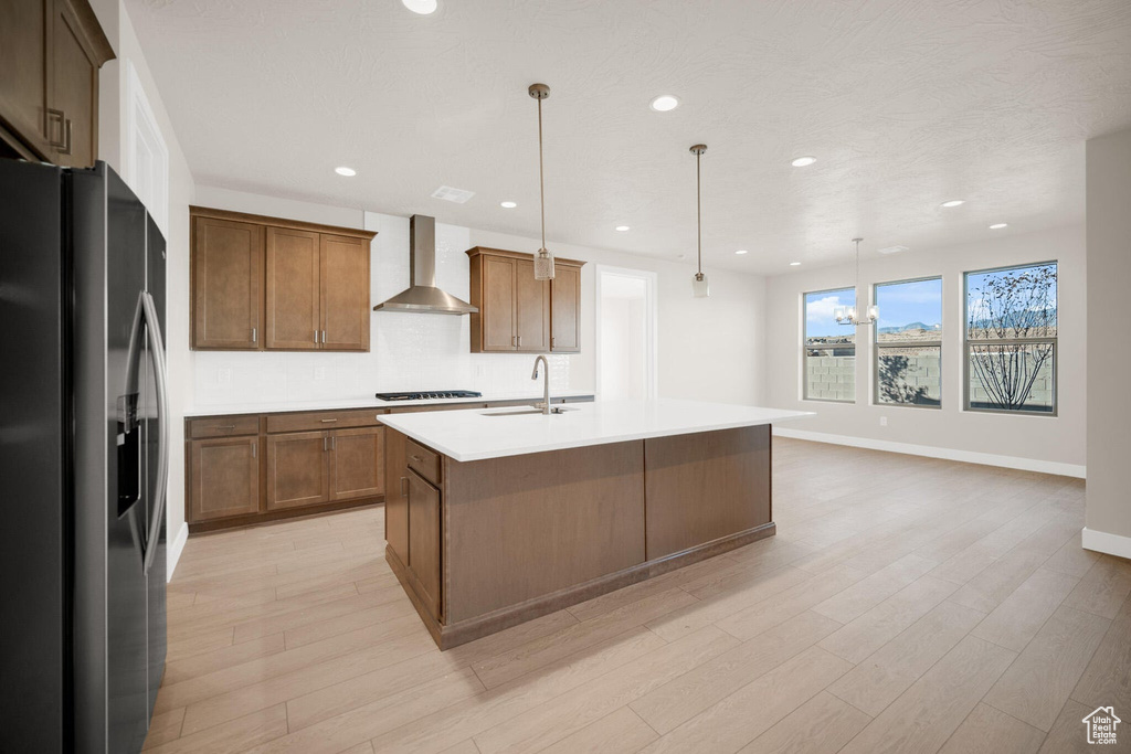 Kitchen with stainless steel refrigerator with ice dispenser, wall chimney exhaust hood, a sink, stovetop, and light countertops