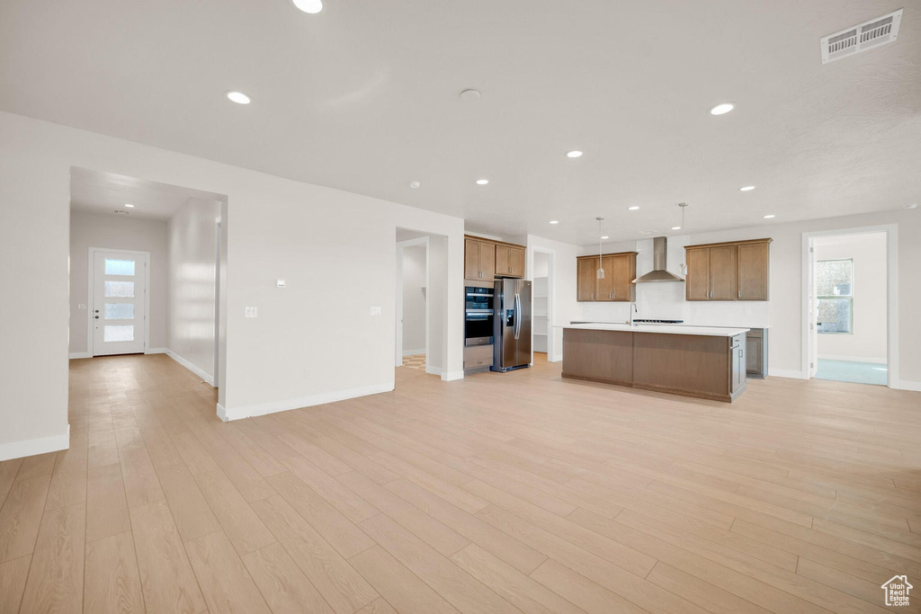 Kitchen with open floor plan, stainless steel appliances, wall chimney range hood, baseboards, and recessed lighting
