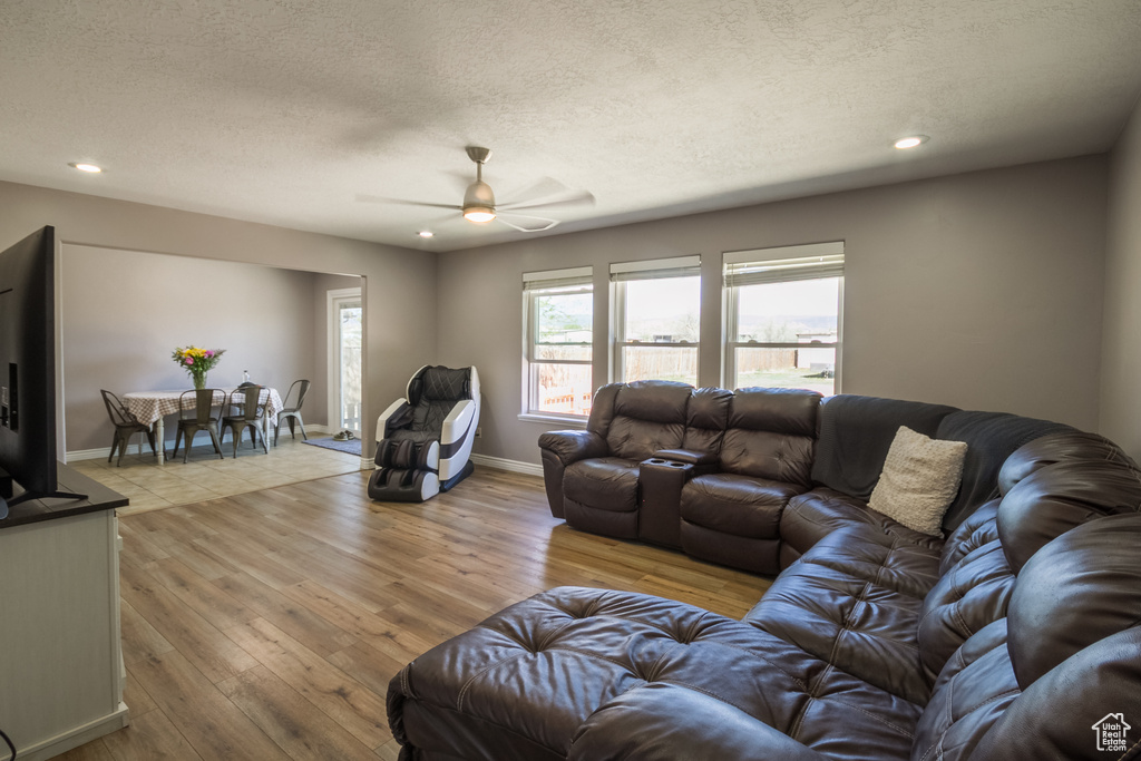 Living area featuring light wood finished floors, a textured ceiling, a ceiling fan, recessed lighting, and baseboards