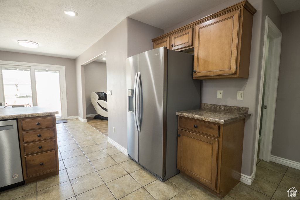 Kitchen featuring stainless steel appliances, brown cabinets, baseboards, light tile patterned floors, and recessed lighting