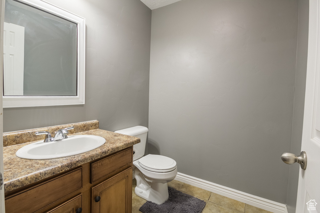 Half bath with toilet, vanity, tile patterned flooring, and baseboards