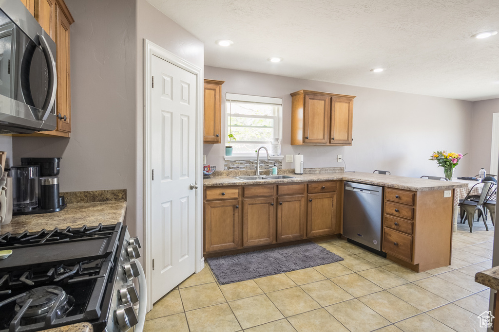 Kitchen featuring appliances with stainless steel finishes, a sink, a peninsula, brown cabinetry, and recessed lighting