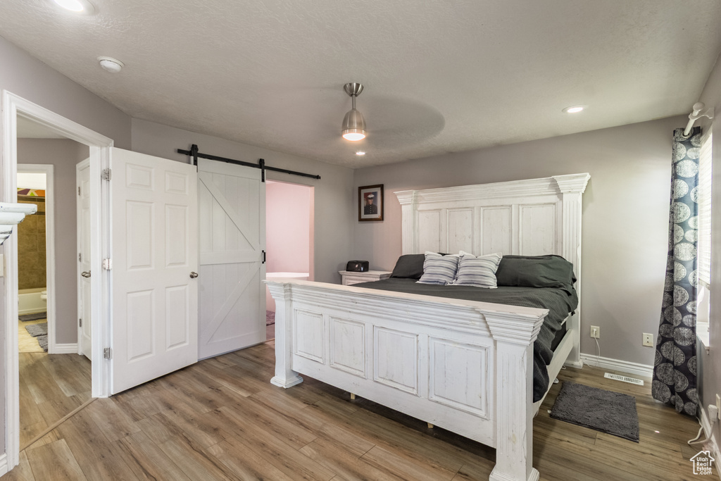 Bedroom with a barn door, light wood-style floors, baseboards, recessed lighting, and a ceiling fan