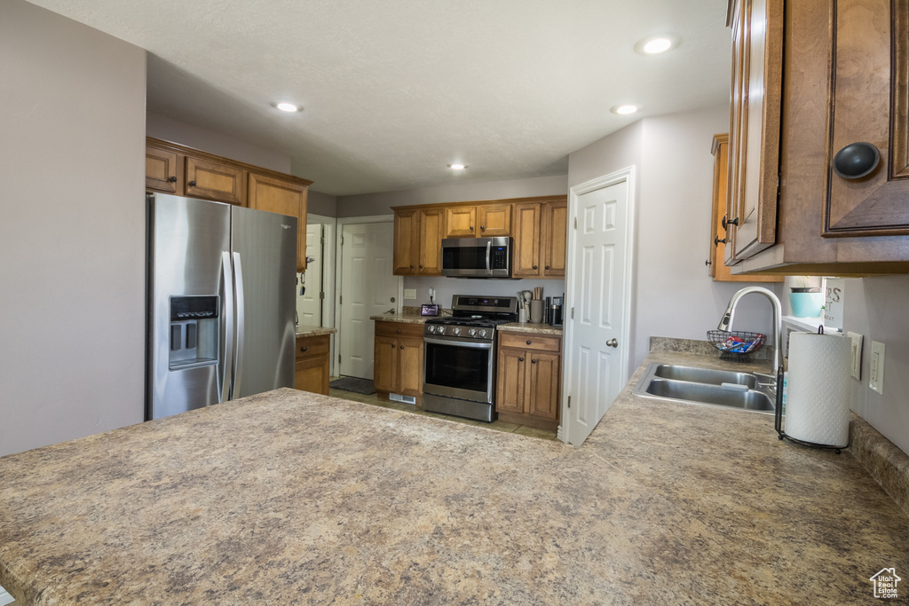 Kitchen featuring stainless steel appliances, a sink, brown cabinets, recessed lighting, and a peninsula