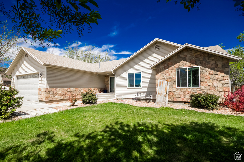 Ranch-style home featuring stone siding, an attached garage, a front lawn, and driveway