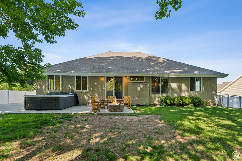 Back of property featuring a fire pit, a hot tub, a patio, and roof with shingles