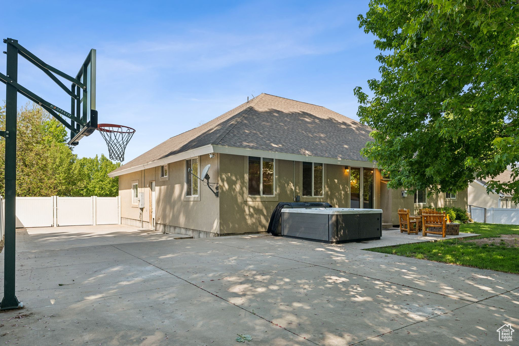 Rear view of property featuring a hot tub, roof with shingles, and a patio area