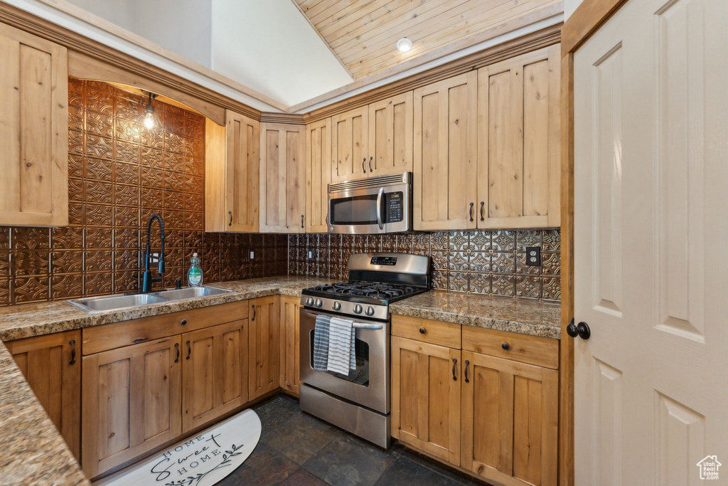 Kitchen featuring stainless steel appliances, a sink, decorative backsplash, light brown cabinetry, and lofted ceiling