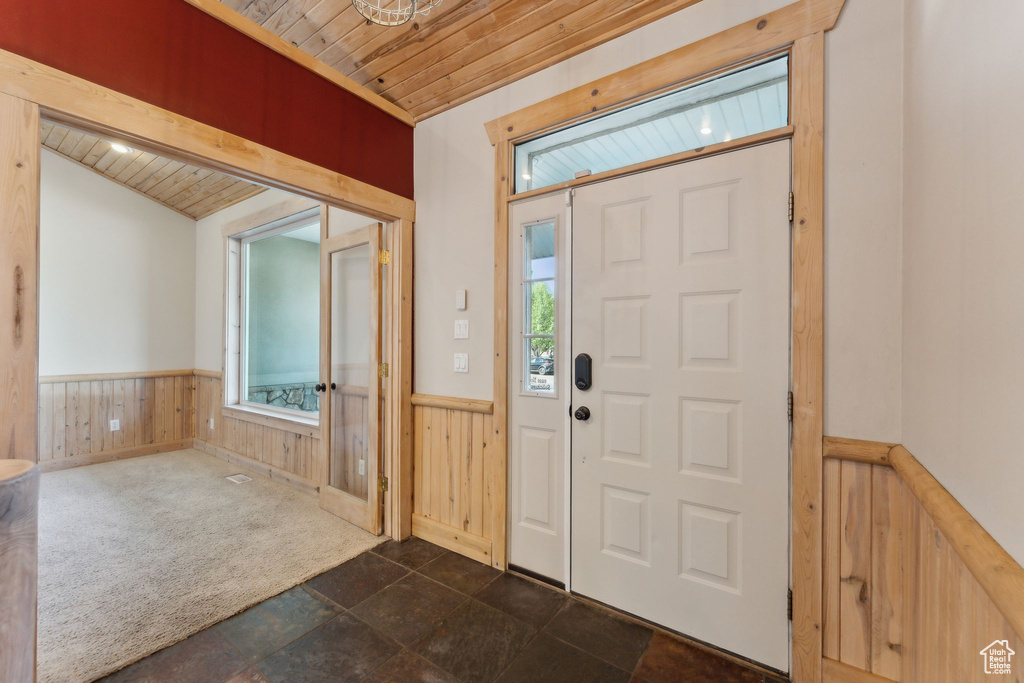 Entrance foyer featuring wooden ceiling, healthy amount of natural light, wainscoting, wood walls, and dark stone finish floors