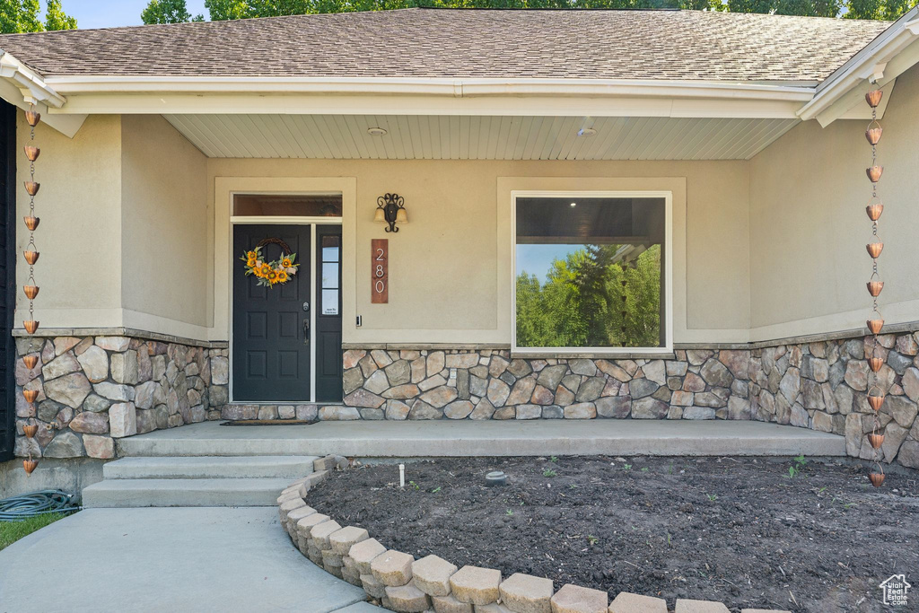 View of exterior entry featuring stone siding, stucco siding, and roof with shingles