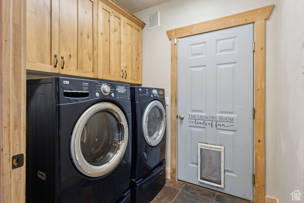 Laundry room featuring washing machine and clothes dryer, stone tile floors, and cabinet space