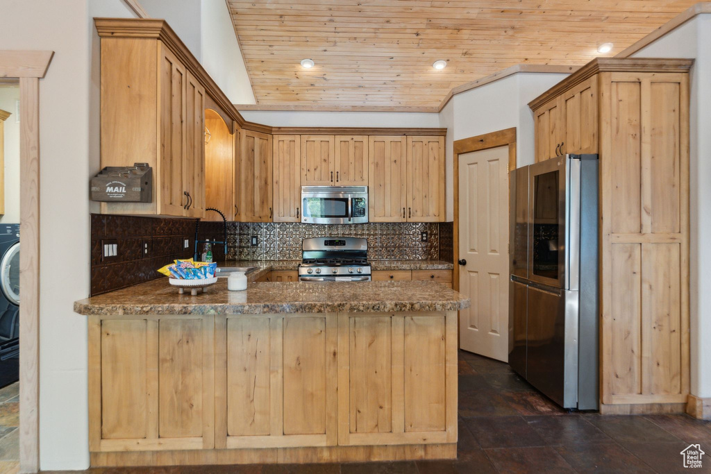 Kitchen with appliances with stainless steel finishes, a peninsula, backsplash, wooden ceiling, and dark stone countertops