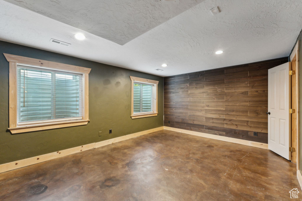 Empty room featuring wood walls, finished concrete floors, recessed lighting, plenty of natural light, and a textured ceiling