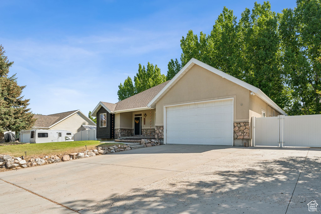 Ranch-style home with stone siding, an attached garage, a gate, driveway, and stucco siding