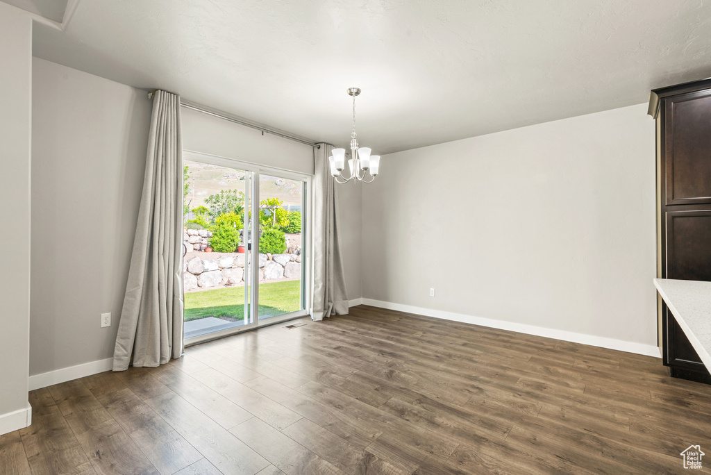 Unfurnished room with dark wood-type flooring, a chandelier, and baseboards