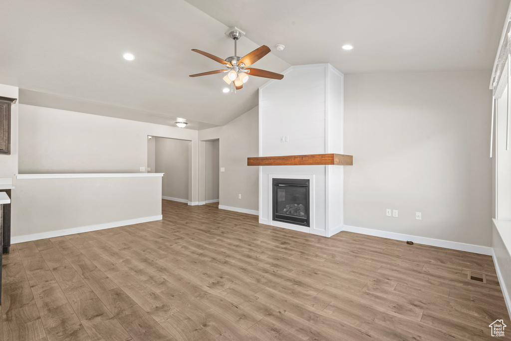 Unfurnished living room featuring ceiling fan, a fireplace, wood finished floors, lofted ceiling, and baseboards