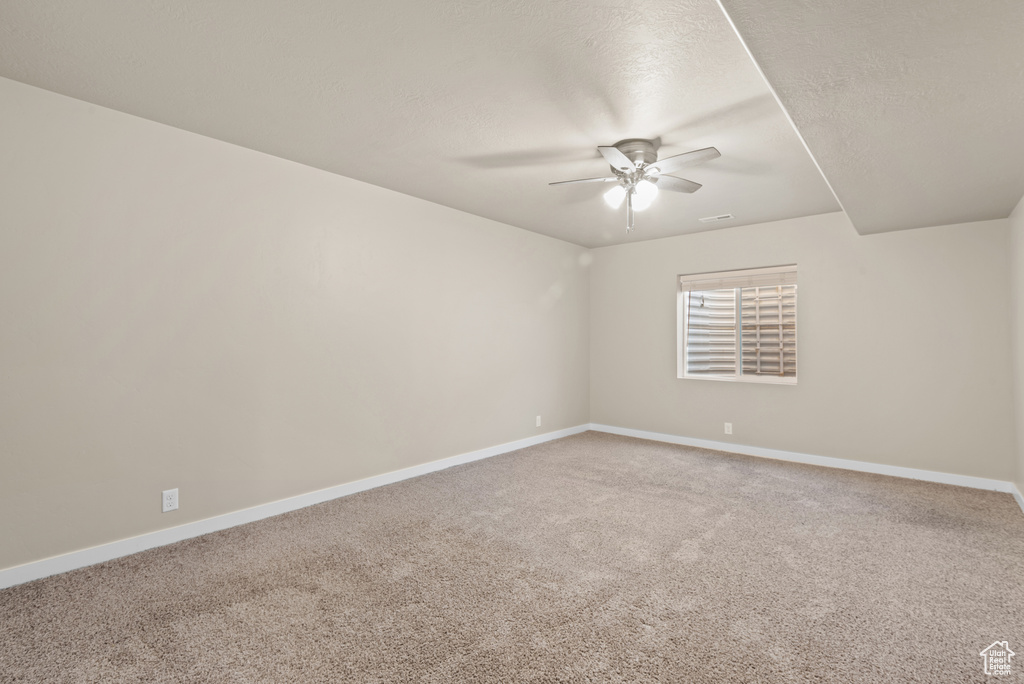 Carpeted spare room with a ceiling fan and baseboards