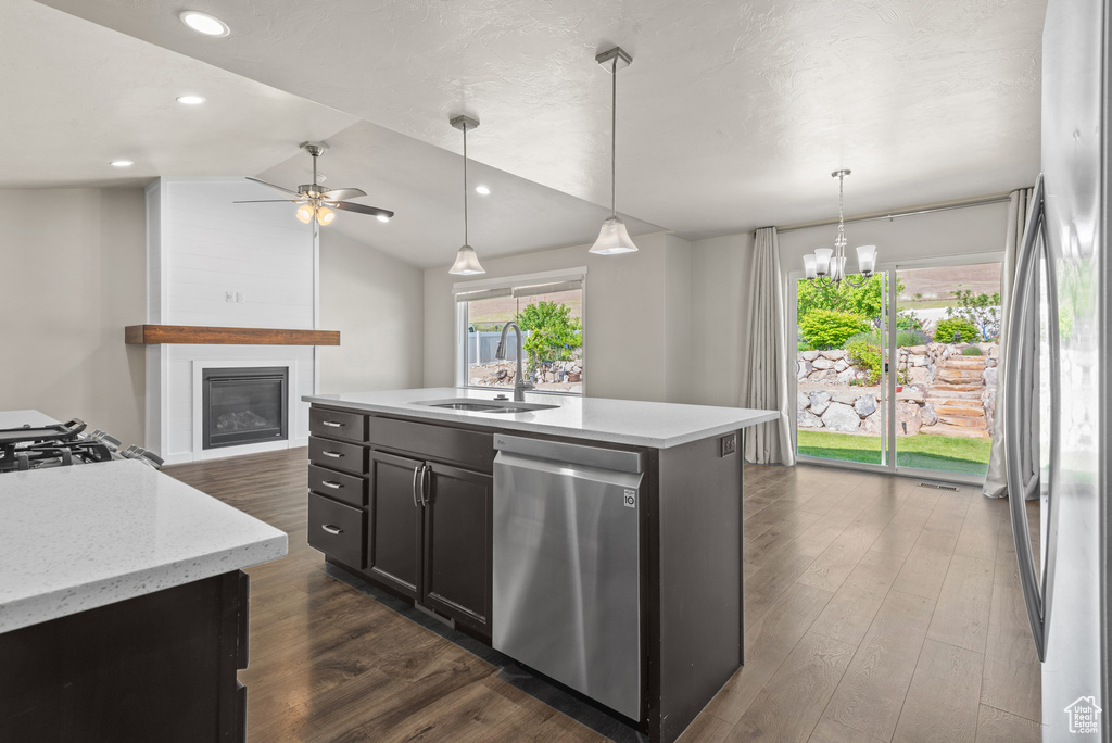 Kitchen featuring appliances with stainless steel finishes, a sink, a large fireplace, dark wood finished floors, and vaulted ceiling