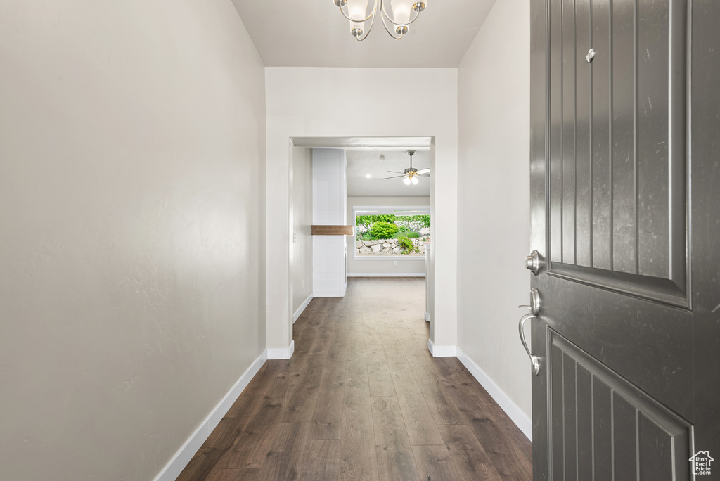 Hallway with baseboards, dark wood-style flooring, and a chandelier
