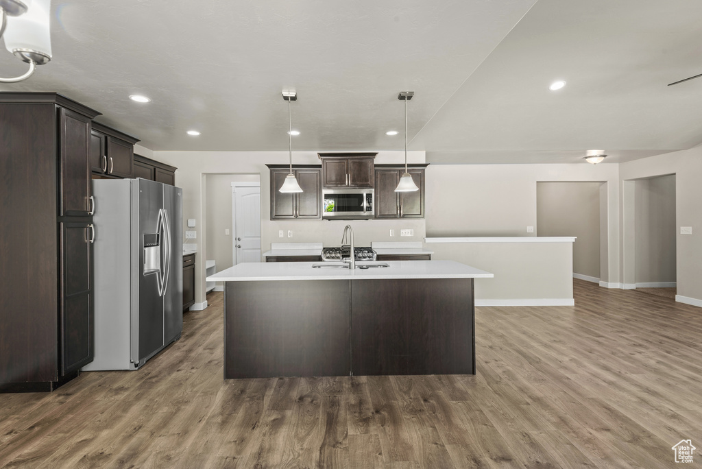 Kitchen featuring appliances with stainless steel finishes, dark brown cabinetry, light countertops, wood finished floors, and recessed lighting