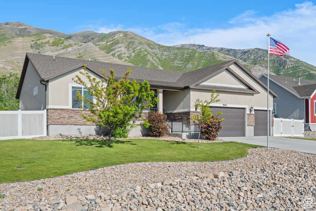 Ranch-style house with stucco siding, stone siding, driveway, an attached garage, and a mountain view