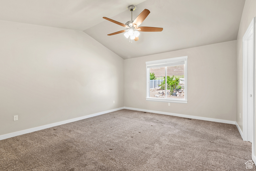 Carpeted empty room with vaulted ceiling, ceiling fan, and baseboards