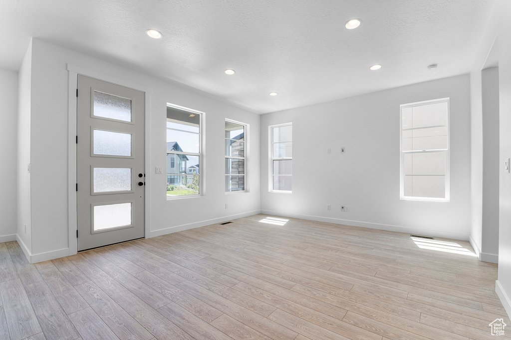 Unfurnished living room with light wood-type flooring, plenty of natural light, baseboards, and recessed lighting