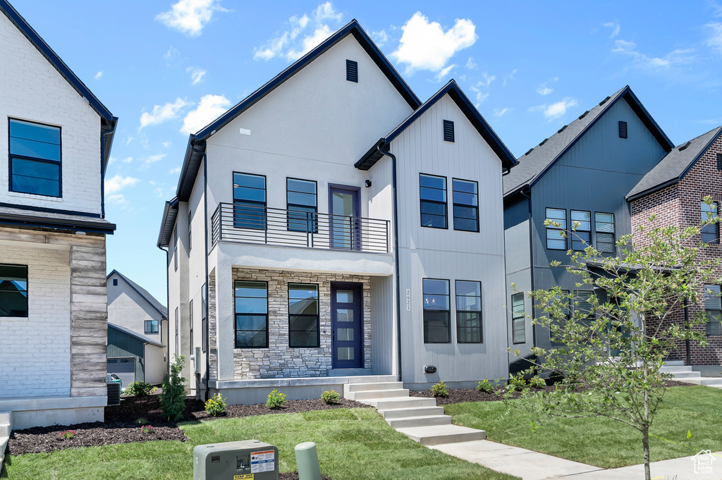 View of front facade featuring a balcony, a front yard, and stone siding