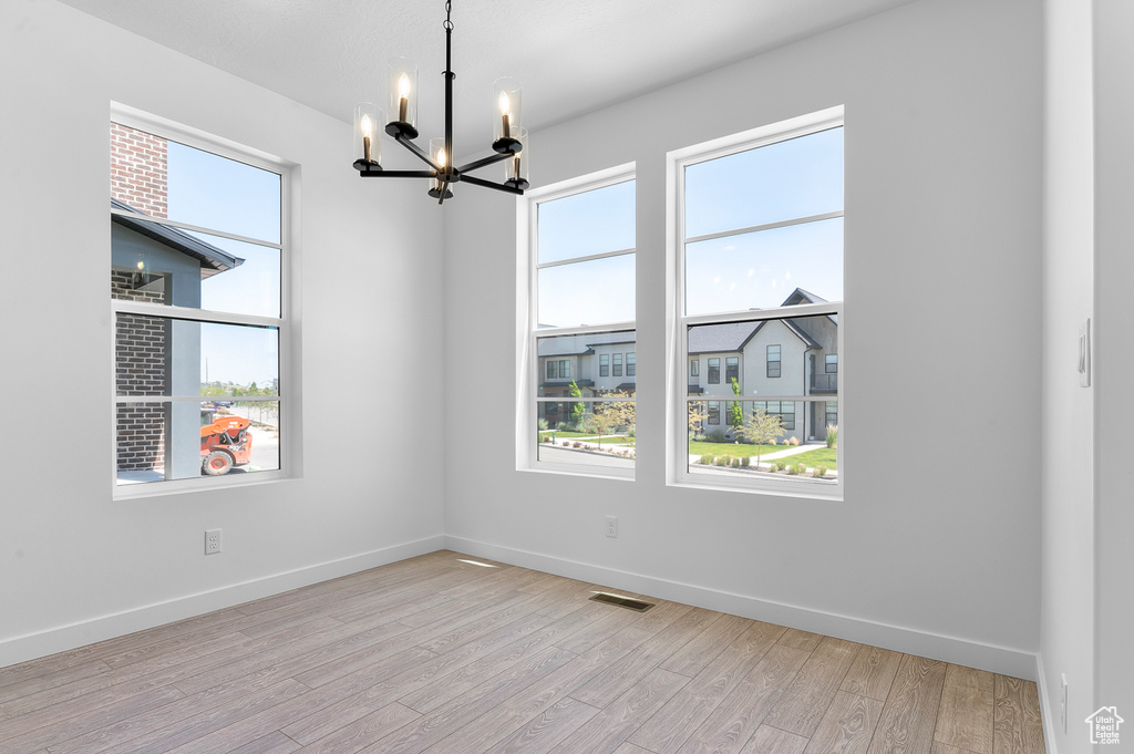 Unfurnished room with a chandelier, light wood-type flooring, and baseboards